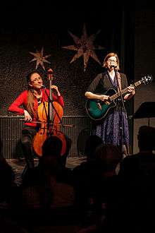 Photograph of the sisters; Aubrey on the left playing a cello and Angela on the right playing a guitar.
