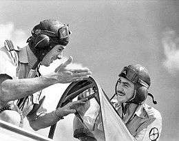 Two men in flying goggles talking beside an aircraft cockpit