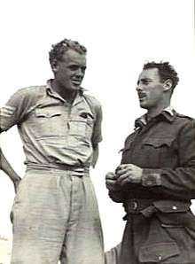 Two men talking, one in light-coloured military fatigues, the other in a dark-coloured battle jacket