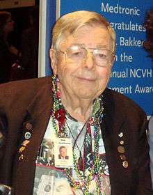 waist-high portrait, wearing Hawaiian shirt, brown suitcoat and necklaces