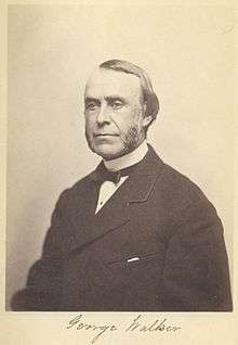 A browning black and white photograph of George Walker, a man with a high hairline and part and mutton chops wearing a band collar, small back bow tie and heavy dark suit jacket