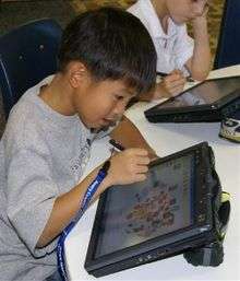  A young Asian boy in a gray T-shirt at a round table using a tablet computer