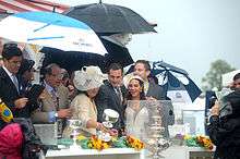 Happy group of people standing under umbrellas looking at silver trophies