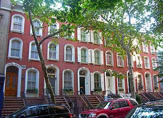 A row of three-story brick townhouses with arched windows and two trees in front