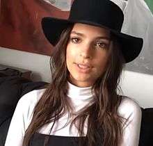 Brunette white woman with a black hat in a white turtleneck with dark overalls