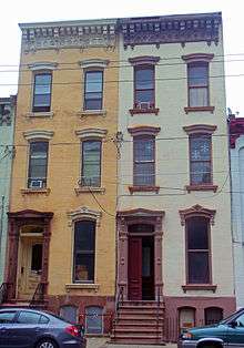 Two narrow three-story tall brick rowhouses painted different shades of yellow but otherwise identical