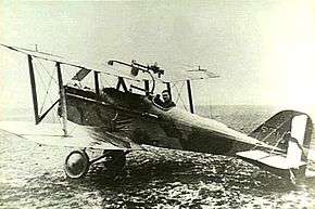 Side view of military biplane with pilot in cockpit, parked on an airfield