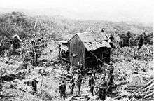 Soldiers stand in front of a dilapidated shed