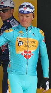 A man wearing a blue and yellow cycling jersey while standing.