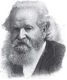 A man with long gray hair, a mustache, and a long gray beard wearing a black jacket and white shirt