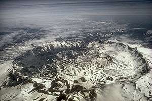 Aerial view of large, snowy crater, surrounded by mountains