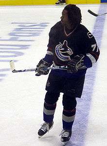 Hockey player in dark blue uniform with his helmet off. He skates on the ice, his stick held off the ground.