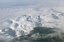  Aerial view of a range of icy mountains with a coastline visible in the foreground