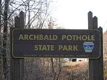 A wooden sign reads "Archbald Pothole State Park" with "Department of Conservation and Natural Resources" in smaller letters below, and a keystone shaped seal reading "Pennsylvania State Parks DCNR" at right