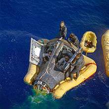 Photo of Armstrong and Scott in the Gemini capsule, in the water. They are being assisted by some recovery crew