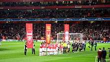 A line of people on a field, behind them are three red banners.UEFA Champions League quarter-final
