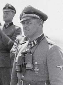 A man wearing a military uniform, peaked cap and a neck order in the shape of a cross.