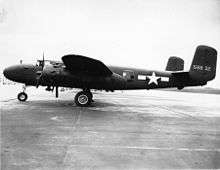 Black and white photo of an early bomber parked perpendicular to camera, facing left. Rearward of the wing is a star in front of horizontal stripes.