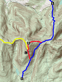 A topographic map of Balsam Lake Mountain with brown contour lines on a green and white background. Red, yellow and blue lines indicate the trails, with black-and-white pictograms denoting the fire tower, lean-to and trailhead facilities