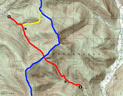 A green topographic map with brown contour lines showing Balsam Mountain with Big Indian Hollow on the east. Winding red and blue lines intersect below the summit, and a short yellow line connects them in the upper left quadrant