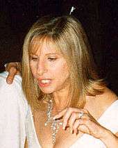 A woman with blond hair, wearing a white dress and jeweled necklace.