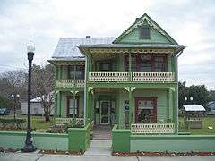 a two story green house with Victorian ornamentation