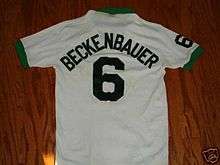 A white soccer jersey, viewed from the back; the cuffs and collar are green and on the back it is marked with the number 6 and the name "Beckenbauer".