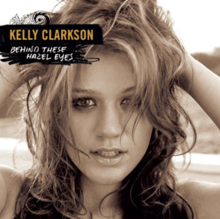 A black and white frontal image of Clarkson holding her curly hair at the back of her head. She is looking in front. On her upper left, the word "Kelly Clarkson" and "Behind These Hazel Eyes" are written in yellow and white capital letters respectively.