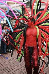 bare-chested man, his skin painted red, with balloons on his back to look like tentacles