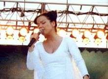 A photo of Björk on stage dressed in white singing into a hand held microphone.