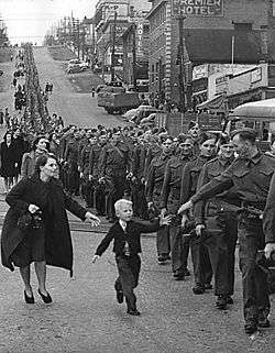 soldiers marching down a road with a boy reaching for them