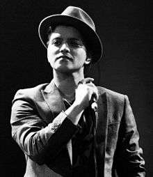 A black and white photograph of Bruno Mars performing with his band at a concert.