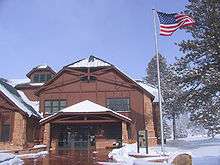 Two story wood building next to flag pole with U.S. flag waving in the wind. Snow on ground.