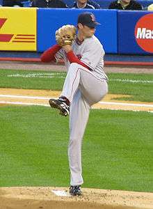 A man in a gray baseball uniform winds up to pitch with his right hand.