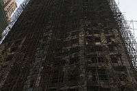 An upward view of a burned-out high-rise: a blackened mess of tangled scaffolding and holes for windows.