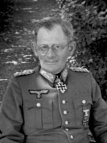 A man wearing a military uniform and glasses with an Iron Cross displayed at the front of his uniform collar.