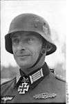 Black-and-white portrait of a man wearing a steel helmet, military uniform with an Iron Cross displayed at his neck.