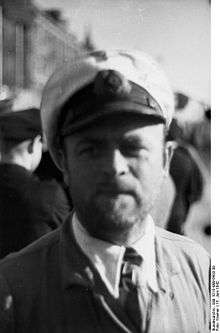 A bearded man wearing a white peaked cap, and an Iron Cross displayed at the front of his uniform collar.