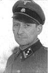A man wearing a military uniform and peaked cap. His cap has an emblem in shape of a human skull and crossed bones.