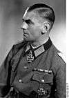 A man wearing a military uniform, facing left of the viewer. Dressed in German World War II Officer uniform with a neck order in the shape of a cross.