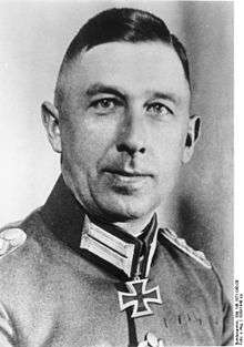A black-and-white photograph of a man in semi profile wearing a military uniform and a neck order in shape of an Iron Cross. His hair appears blond and is combed back.