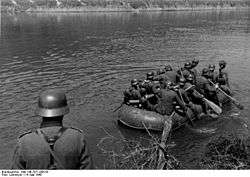 a black and white photograph of a group of German soldiers paddling a rubber boat across a river