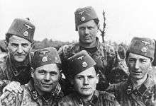 a black and white photograph of men wearing Waffen-SS camouflage jackets and a fez