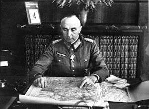 male officer in uniform sitting at a desk looking at a map