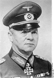 A man wearing a peaked cap, military uniform with an Iron Cross displayed at the front of his uniform collar.