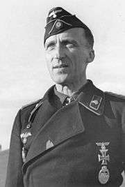 A black-and-white photograph of a man wearing a dark military uniform, side cap and a neck order in shape of an Iron Cross.