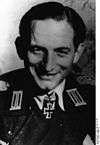 A black-and-white photograph of a smiling man wearing a military uniform and neck order in shape of an Iron Cross. His hair is combed back.