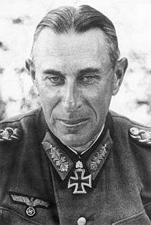 The head and shoulders of an elderly man, shown from the front. He wears a military uniform with an Iron Cross displayed at the front of his collar. His hair is parted, combed back and appears either dark or grey, his facial expression is a determined and grim; his eyes are looking into the camera.