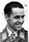 A smiling man wearing a military uniform with an Iron Cross displayed at the front of his uniform collar.