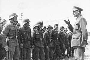 a black and white photograph of a bespectacled Andrey Vlasov in German uniform addressing some soldiers